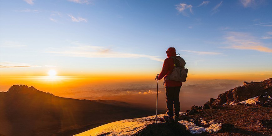 Mann steht bei Sonnenaufgang auf dem Kilimandscharo